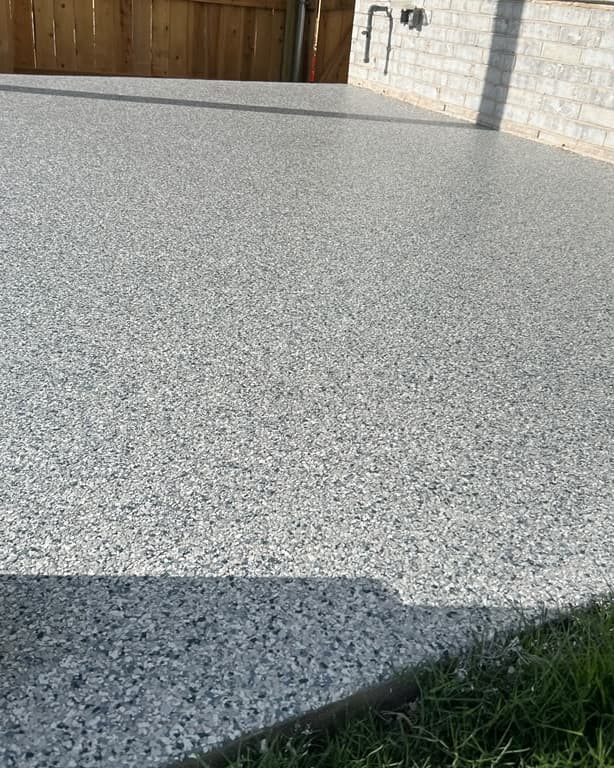 Completed gray textured coating across an exterior concrete surface beside a brick home