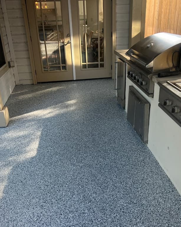 Completed gray patio coating beside an outdoor grill and residential entry